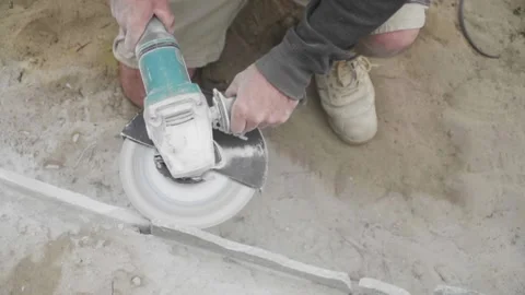 Man kneeling using power tool on construction site, cutting stone paving Stock Footage 133046866