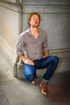 A man kneels on a patterned floor next to a stone wall,  looking up Stock Photos