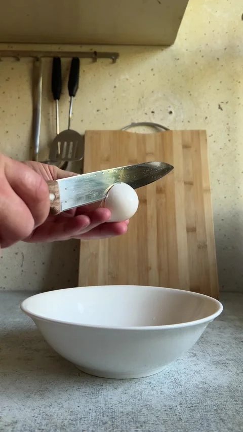 Man with knife breaks chicken egg at kitchen. Yellow yolk falls into white bowl Stock Footage 276970831