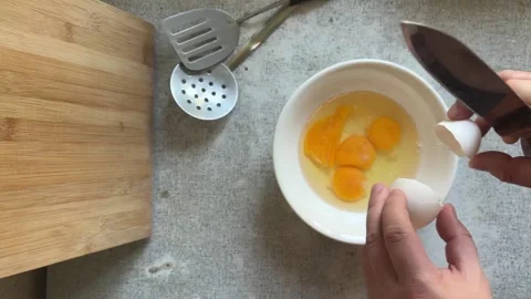 Man with knife breaks chicken egg at kitchen. Yellow yolk falls into white bowl Stock Footage 277173160