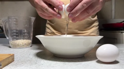 Man with knife breaks chicken egg. Yellow yolk falls into bowl on kitchen table Stock Footage 280915445