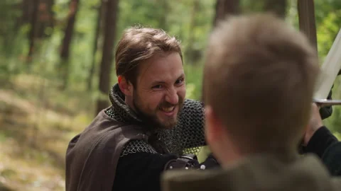 Man in knight armor fights with boy on swords at camp Video stock 218877875