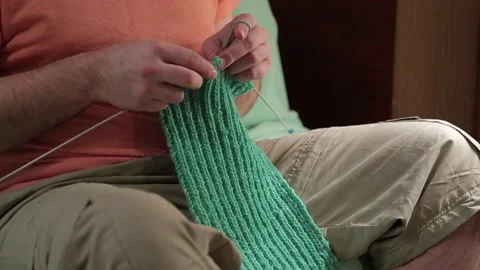  A  man knits a green scarf while sitting in a room on couch. We see only hand Stock Footage 87831787