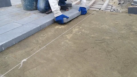 A man knocks on gray rectangular paving slabs, placing them on a sand - 23s Stock Footage 120026377