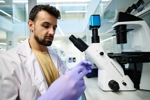 Man in lab coat examining samples under an inverted microscope Фото