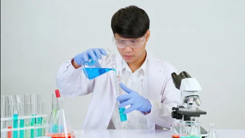 Man in lab coat pouring solution into cylinder Видео 201725612