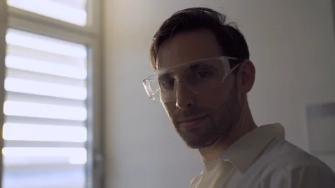 Man with lab glasses looking at camera standing next to lab or hospital window Stock Footage 112619313