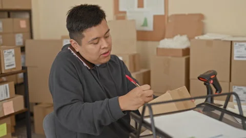 Man labeling a parcel with a red pen while holding smartphone between ear a.. Video stock 337355891