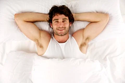 Man laid in white bed looking up at the camera smiling Fotos de archivo
