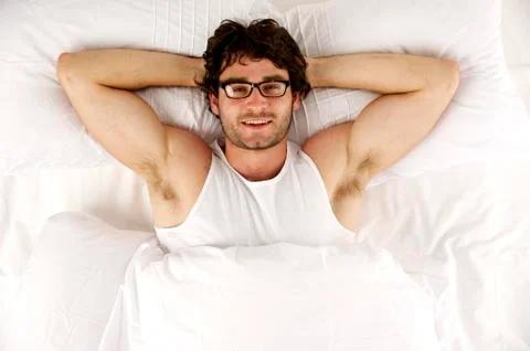 Man laid in white bed looking up at the camera smiling Stock Photos