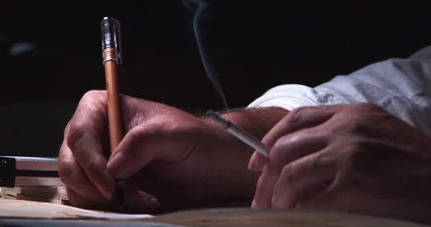 A man in lamplight, smoking a cigarette, processing information from a Stock Footage 201598458