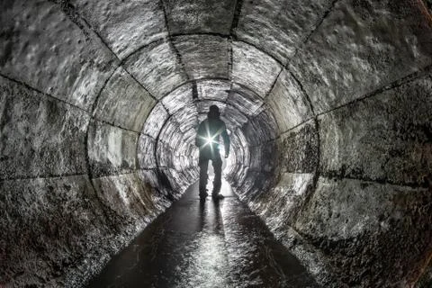 Man with a lantern in an underground round concrete rain collector. Stock Photos