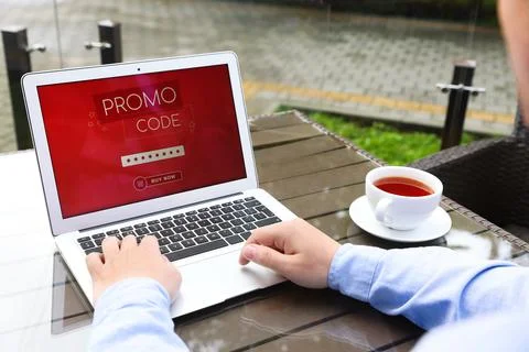 Man with laptop activating promo code at wooden table outdoors, closeup Stock Photos
