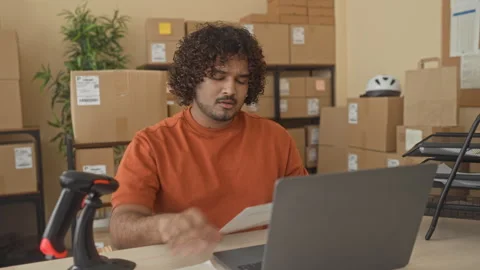 Man at laptop holding papers in building amid stacked cardboard boxes and b.. Stock Footage 337395366