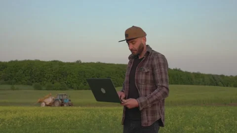 A man with a laptop monitors the work of a tractor in the field. Stock Footage 251112133