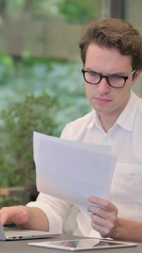 Man with Laptop Reading Documents in Modern Office, Vertical Video Stock Footage 340032541