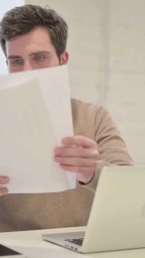 Man with Laptop Reading Documents in Office, Vertical Video 스톡 동영상 337351196