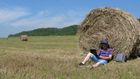 A man with a laptop sits by a haystack. Stock Footage 135594047