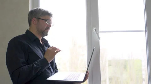 A man with a laptop by the window. Video Conversations 4K Stock Footage 129529521