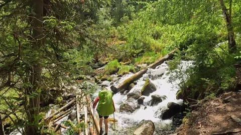 Man with a large backpack crosses a wide mountain stream Stock Footage 246291868