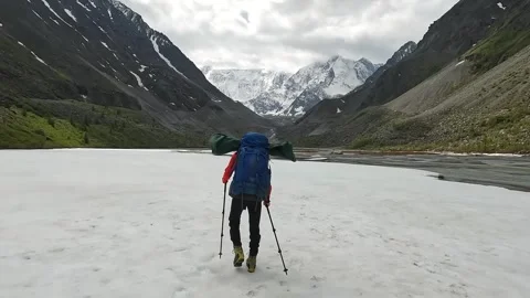 Man with a large backpack walks along the snowy slope along the river Video stock 246292201
