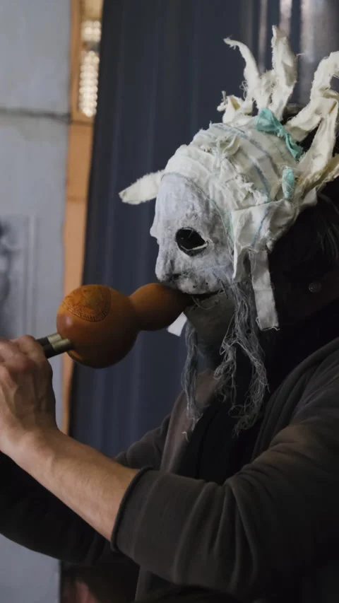 Man in large mask plays wind instrument leaning forward 스톡 동영상 316144723