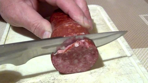 A man with a large sharp knife cuts hard sausage into circles on a cutting board Stock Footage 155426965