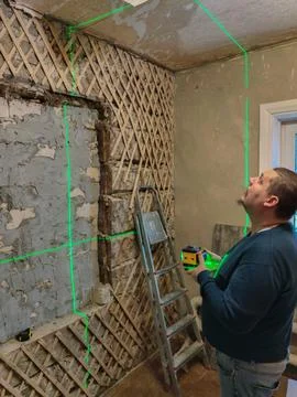 A man with a laser level projects bright green horizontal and vertical lines Stock Photos