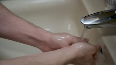 A man lathers his hands with soap under the running water of the bathroom sink Stock Footage 257371754