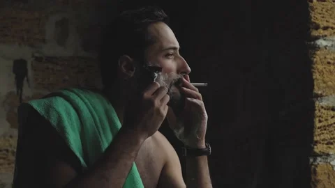 A man of Latin appearance smokes and smears shaving foam on his face. The man is Stock Footage 151753699