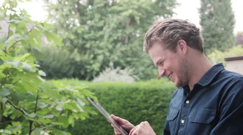 Man laughing, using tablet in garden Stock Footage 40661993