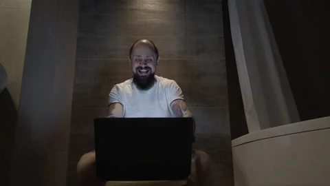 A man laughs sitting at a computer in the toilet Stock Footage 133813660