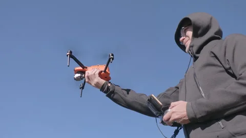 Man launches orange drone into clear blue sky, holding remote control device Stock Footage 338256975