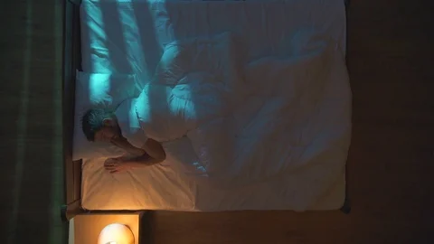 The man lay on a bed and turn off the lamp. Night time. View from above Stock Footage 71964883