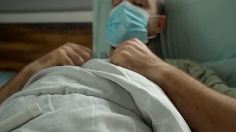 Man laying in bed being sick wearing surgical mask Stock Footage 128294298