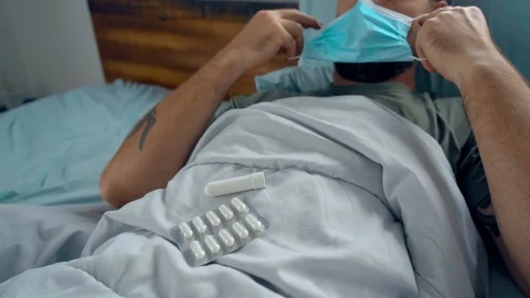 Man laying in bed being sick checking his medicine 스톡 동영상 128294342