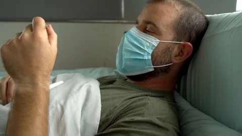 Man laying in bed being sick wearing surgical mask Stock Footage 128294383