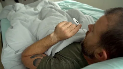 Man laying in bed being sick checking his temperature Stock-Footage 128294452