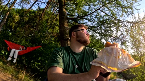 Man laying down in hammock on sunset eating burger Stock-Footage 255203388