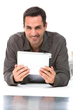 Man laying on the floor, smiling at camera and holding his digital tablet wit Stock Photos