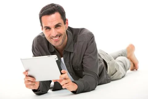 Man laying on the floor, smiling at camera and holding his digital tablet wit Stock Photos