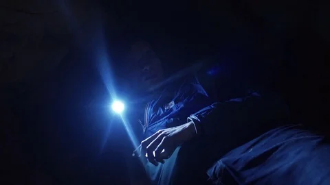 Man laying on ground into narrow cave explores cave walls with hand flashlight Stock Footage 80063254