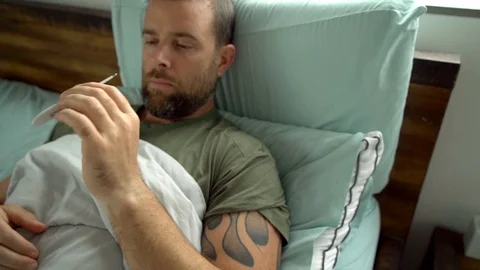 Man laying in Man laying in bed being sick checking his temperature Video stock 128294423