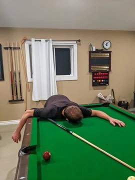 A man lays face down on a pool table 스톡 사진