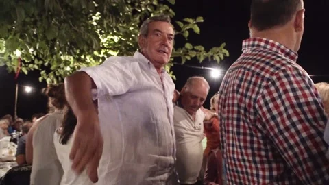 Man leading a group of greeks dancing in a circle with hands on their should Stock Footage 144807269