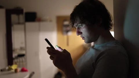 Man leaning against wall stares into smartphone with face glowing purple from sc Stock Footage 313842894
