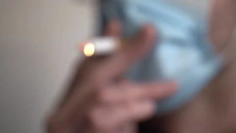 A man leaning forward while smoking through a hole in a face mask 스톡 동영상 132900256