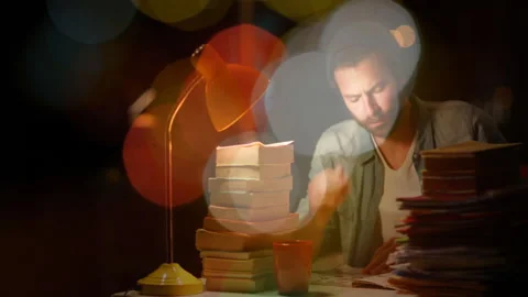 Man leaning on hand studying late in dark room, displaying animated education Stock Footage 307800992