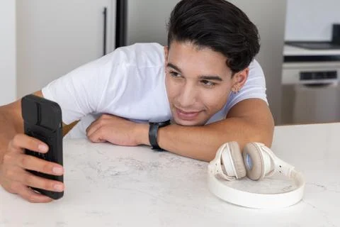 Man leaning on marble-pattern countertop in kitchen, holding black-cased 库存照片