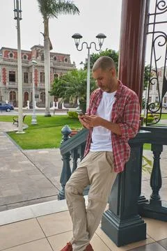 Man leaning on a railing using a mobile phone in a public square Stock Photos